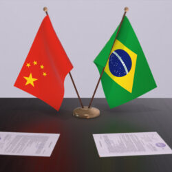Bandeiras da China e do Brasil apoiadas em cima de uma mesa, simbolizando a relação diplomática entre os países.